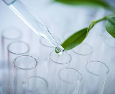 A dropper releasing a liquid droplet above several clear test tubes, with a green leaf partially visible in the background.