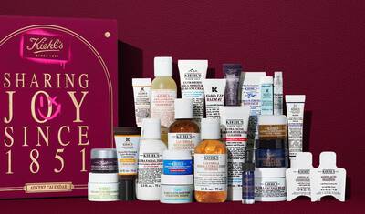 Kiehl's Julekalender gaveaeske i dybrød med guldtekst, vist ved siden af 24 mini hudplejeprodukter, herunder Ultra Facial Cream, Calendula Toner, Retinol Serum og Lip Balm #1. En pink spraymaling-grafik på siden fremhaever saettets vaerdi.
