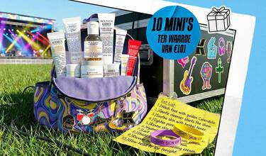 Een promotionele banner van Kiehl's in festivalthema met een kleurrijke reistas vol met 10 mini huidverzorgingsproducten, staand op het gras naast een zwarte flightcase met stickers. Een gele 'Set List' en festivalbandjes liggen op de voorgrond.