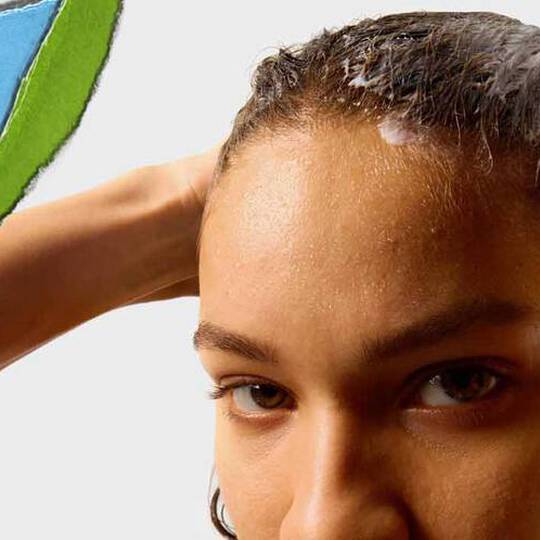 En person med vådt hår påfører et hårprodukt med en farverig, afrevet papirsektion i baggrunden.