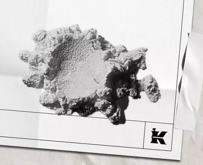 Et struktureret, uregelmaessigt formet hvidt mineral- eller materialefragment, der hviler på en lys baggrund, med et lille logo nederst til højre.