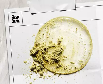 En cirkulaer udtvaering af lys creme med en struktureret bunke grønt pulver, praesenteret på et hvidt ark markeret med et logo.