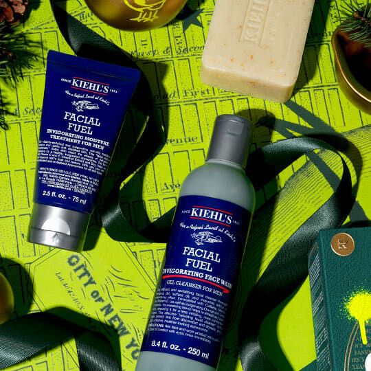 Kiehl's Facial Fuel rensecreme og fugtighedscreme arrangeret med et stykke håndsaebe og grønne juledekorationer på en lys gul baggrund.
