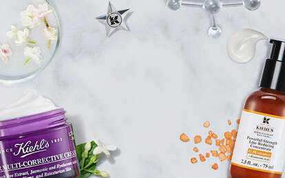 Alt-tekst: Et udvalg af hudplejeprodukter fra Kiehl's, herunder flasker med serummer og en stor creme, praesenteret på en marmoroverflade sammen med blomster og ingredienser.