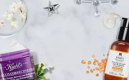 Alt-tekst: Et udvalg af hudplejeprodukter fra Kiehl's, herunder flasker med serummer og en stor creme, praesenteret på en marmoroverflade sammen med blomster og ingredienser.