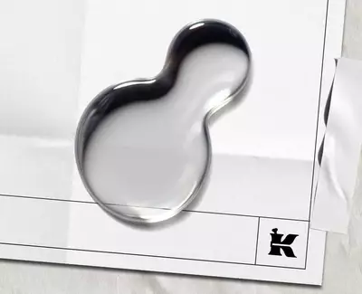 To vanddråber på et blankt stykke papir med et sort "K"-logo og et stykke tape øverst.