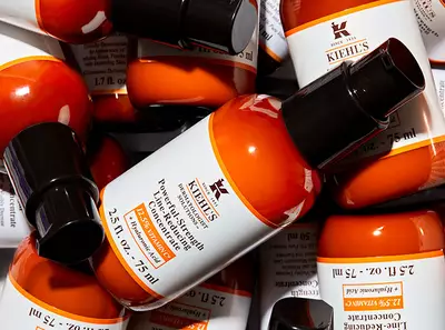 A collection of Kiehl's products featuring orange bottles with black caps, arranged stylishly against a textured background.