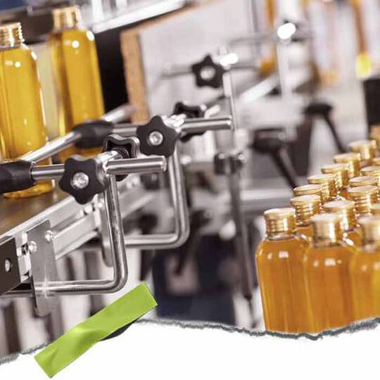 En automatiseret tappelinje med klare flasker fyldt med gul vaeske og metalklemmer, der viser et travlt produktionsmiljø.