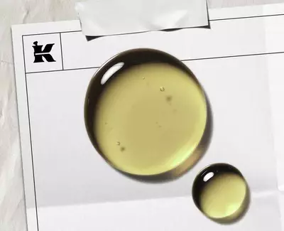 A sliced avocado revealing its seed next to a small glass bowl of golden avocado oil, all set against a rustic wooden background.