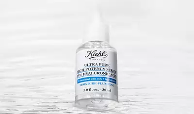 A clear bottle of Kiehl's Ultra Pure High-Potency Serum with 15% hyaluronic acid, featuring a simple white label and blue accents, set against a soft, blurred background.