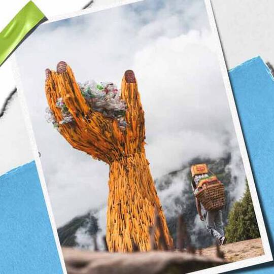 En tårnhøj håndskulptur af trae holder en bunke affald, der symboliserer miljøbevidsthed, med en person, der baerer varer i naerheden.