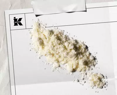 En bunke hvidt pulver på et blankt stykke papir med et logo i hjørnet, hvilket antyder en kunstnerisk eller stilistisk praesentation.