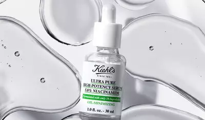 A bottle of Kiehl's Ultra Pure High-Potency Serum with 5% Niacinamide, displayed against a backdrop of smooth, transparent drops of serum. The bottle is clear with a white dropper and a label detailing its formulation.