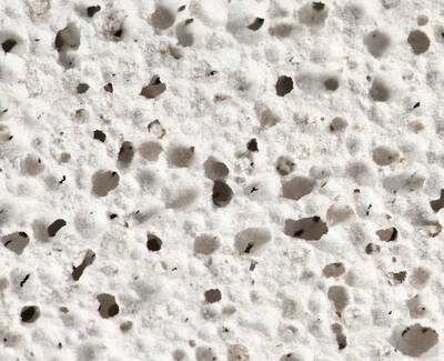 Close-up of a textured, porous white surface with numerous small holes and irregularities.