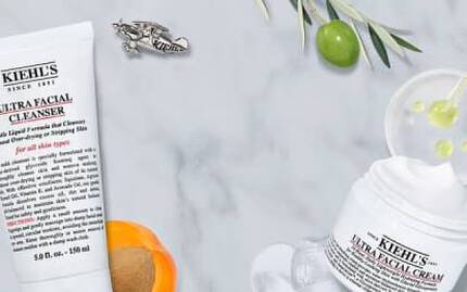 Alt-tekst: Et udvalg af Kiehl's ansigtsplejeprodukter, herunder rensegel, toner og fugtighedscreme, praesenteret på en marmoroverflade med nogle ingredienser og en lille skål.