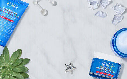 Produkter fra Kiehl's til ansigtspleje, herunder en ansigtsrens, toner, og en ansigtsmaske, praesenteret på en marmoroverflade med citron og isterninger.