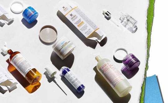 En raekke hudplejeprodukter udstillet på en lys baggrund, herunder flasker, krukker og dråbetaellere i forskellige farver og former.