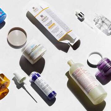 En raekke hudplejeprodukter udstillet på en lys baggrund, herunder flasker, krukker og dråbetaellere i forskellige farver og former.