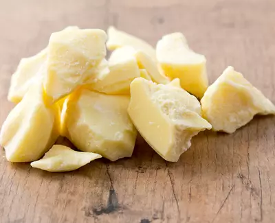Chunks of yellow cocoa butter scattered on a wooden surface.