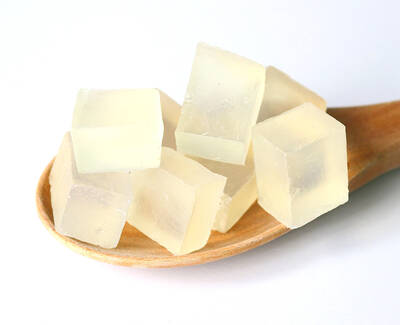 A wooden spoon holds several translucent, pale yellow cubes of gelatin or agar.