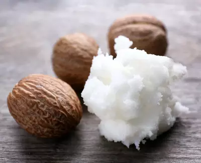 A few whole nutmeg seeds beside a pile of white, soft nutmeg powder on a wooden surface.
