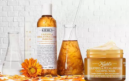 Alt-tekst: Flere hudplejeprodukter fra The Hues på en hvid mur, herunder en olie, en creme og en scrub.
