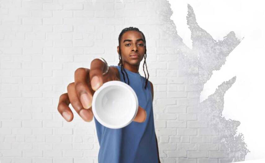 En person i blå aermeløs skjorte holder en lille hvid skål op mod kameraet på en struktureret hvid vaeg.