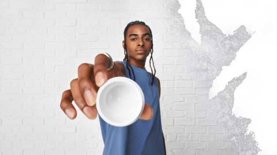 En person i blå aermeløs skjorte holder en lille hvid skål op mod kameraet på en struktureret hvid vaeg.