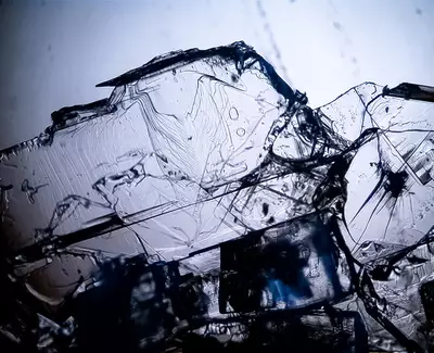 Close-up of transparent crystal formations with intricate textures and reflections, set against a light background.