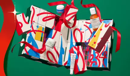 Kiehls jule-adventskalender med nummererede gaveaesker og hudplejeprodukter, indpakket i rødt bånd på en festlig grøn baggrund.
