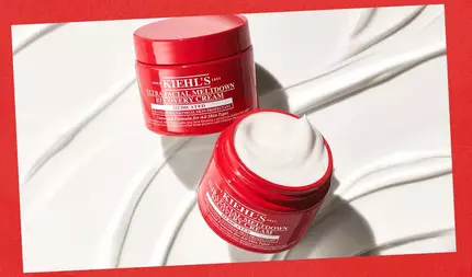 To åbne røde glas med Kiehl's Ultra Facial Meltdown Recovery Cream stod på en hvid tekstureret baggrund med glatte crememønstre, sat mod en rød kant.