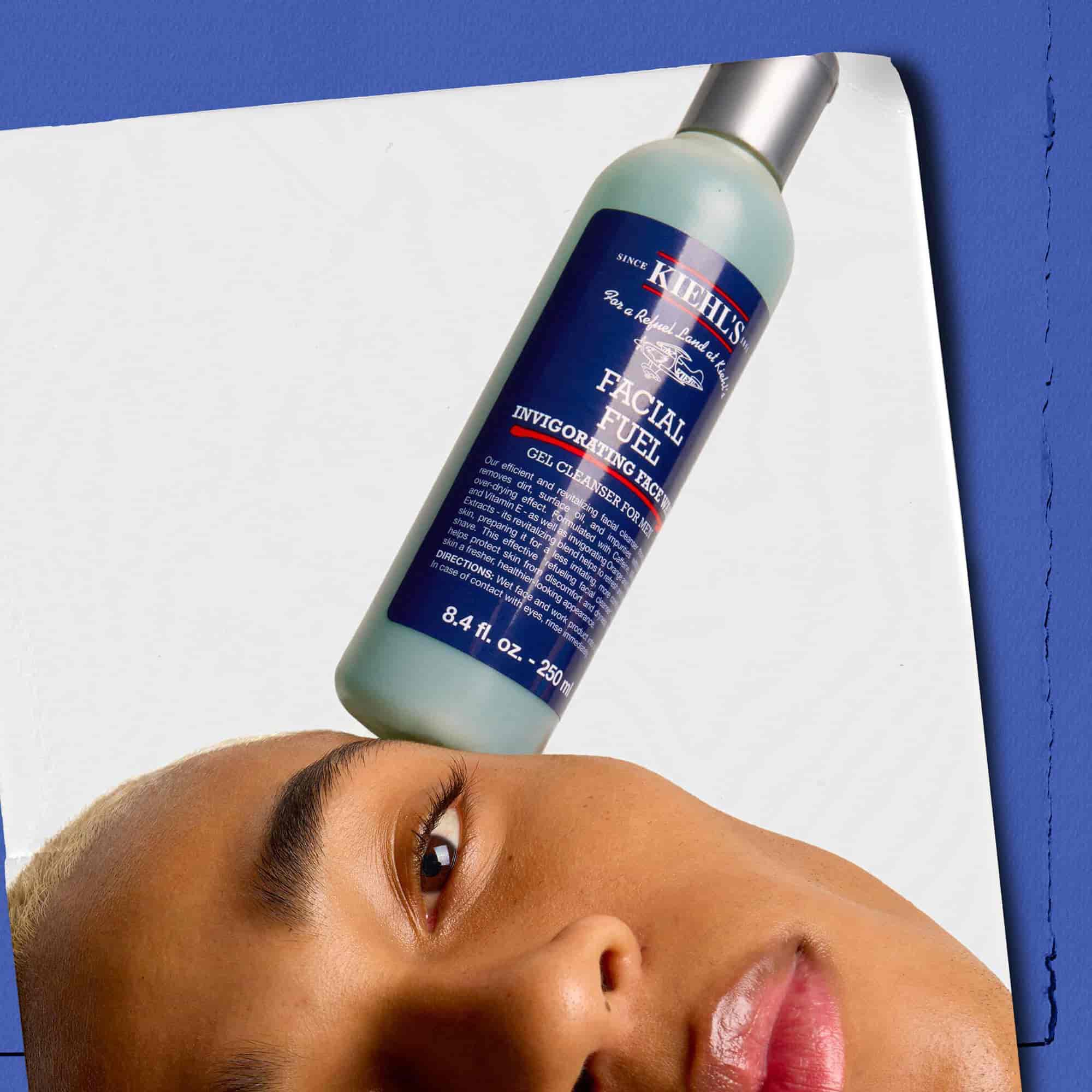 Model med en flaske Kiehl's Facial Fuel Energizing Face Wash balanceret på ansigtet