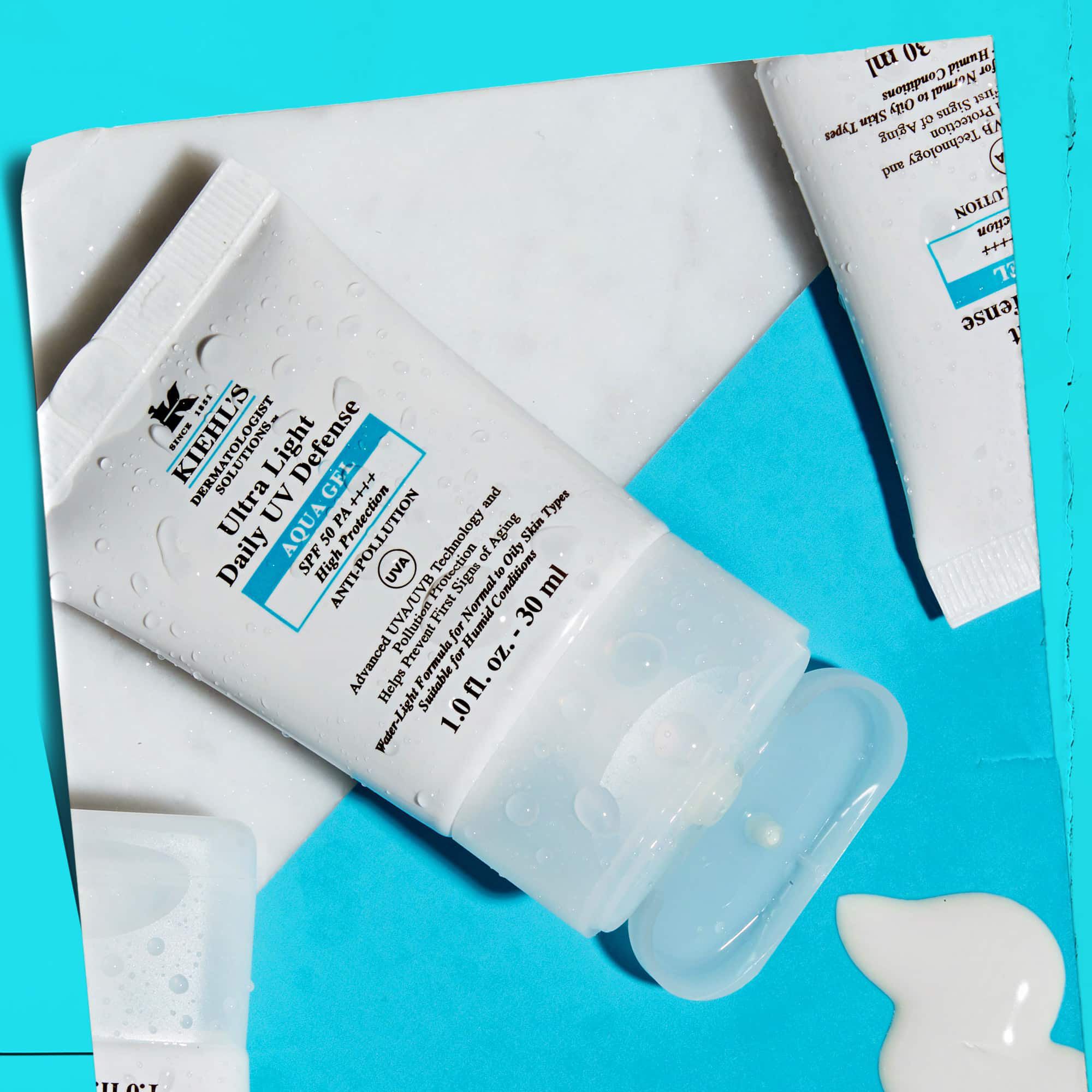 Et flat-lay af flere Ultra Light Daily UV Defense Aqua Gel-tuber på en overflade af marmor, der viser deres livsstilsappel.